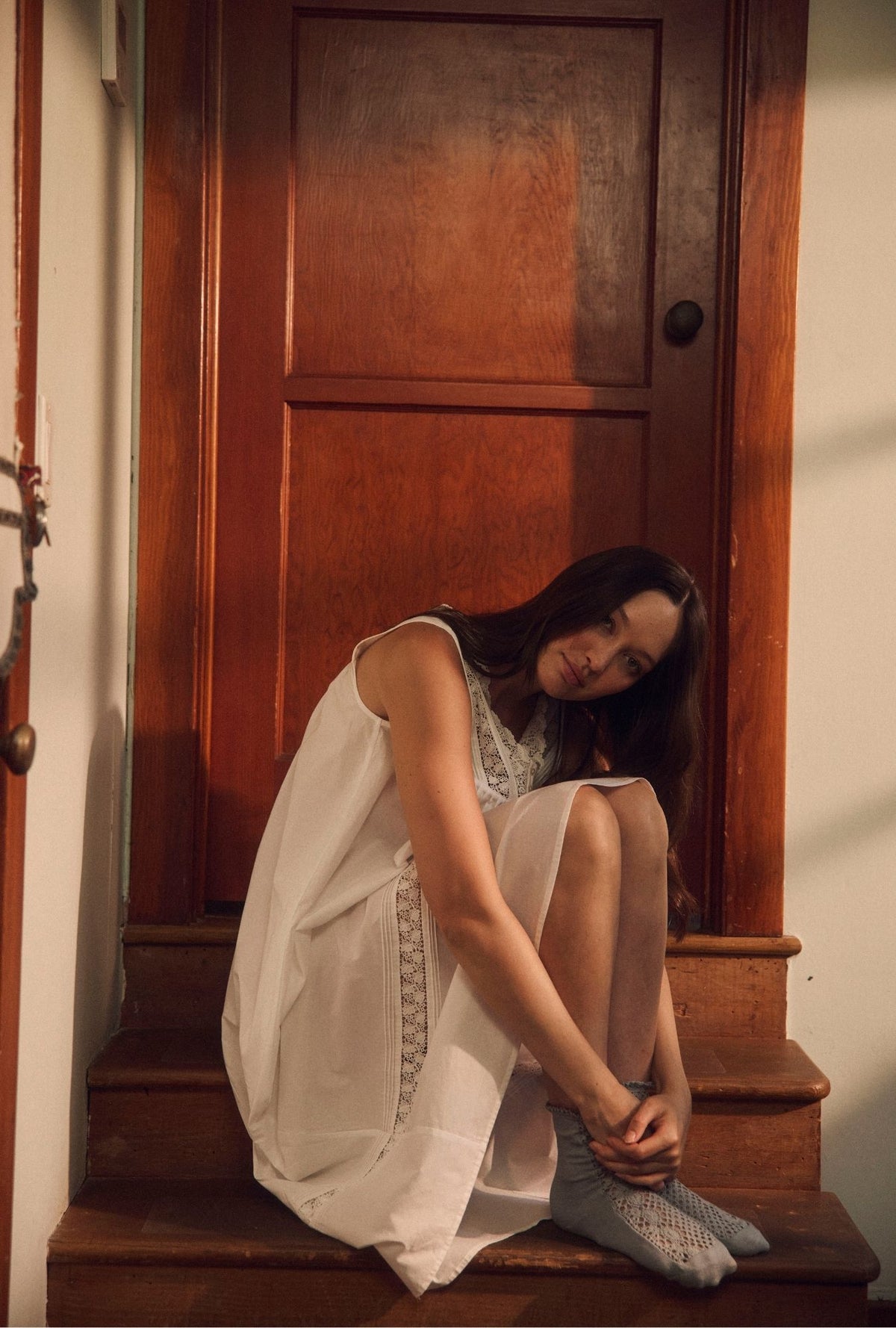 A lady sitting in front of a door wearing a white gown