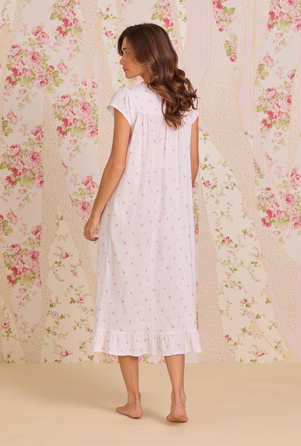 A Lady Wearing Petite Dot Cotton Knit Cap Sleeve Ballet Nightgown facing back pose against a floral wallpaper background, looking to the side