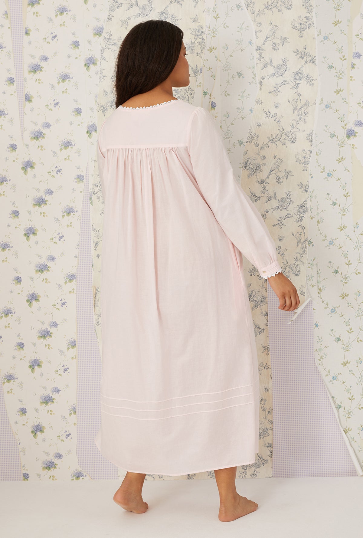 A lady wearing plus size blush Heirloom Dream Long Sleeve Gown in a back view free pose