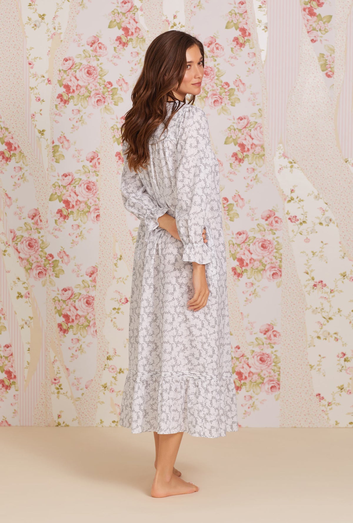 A lady wearing white long sleeve eileen cotton nightgown with grey fleur print.