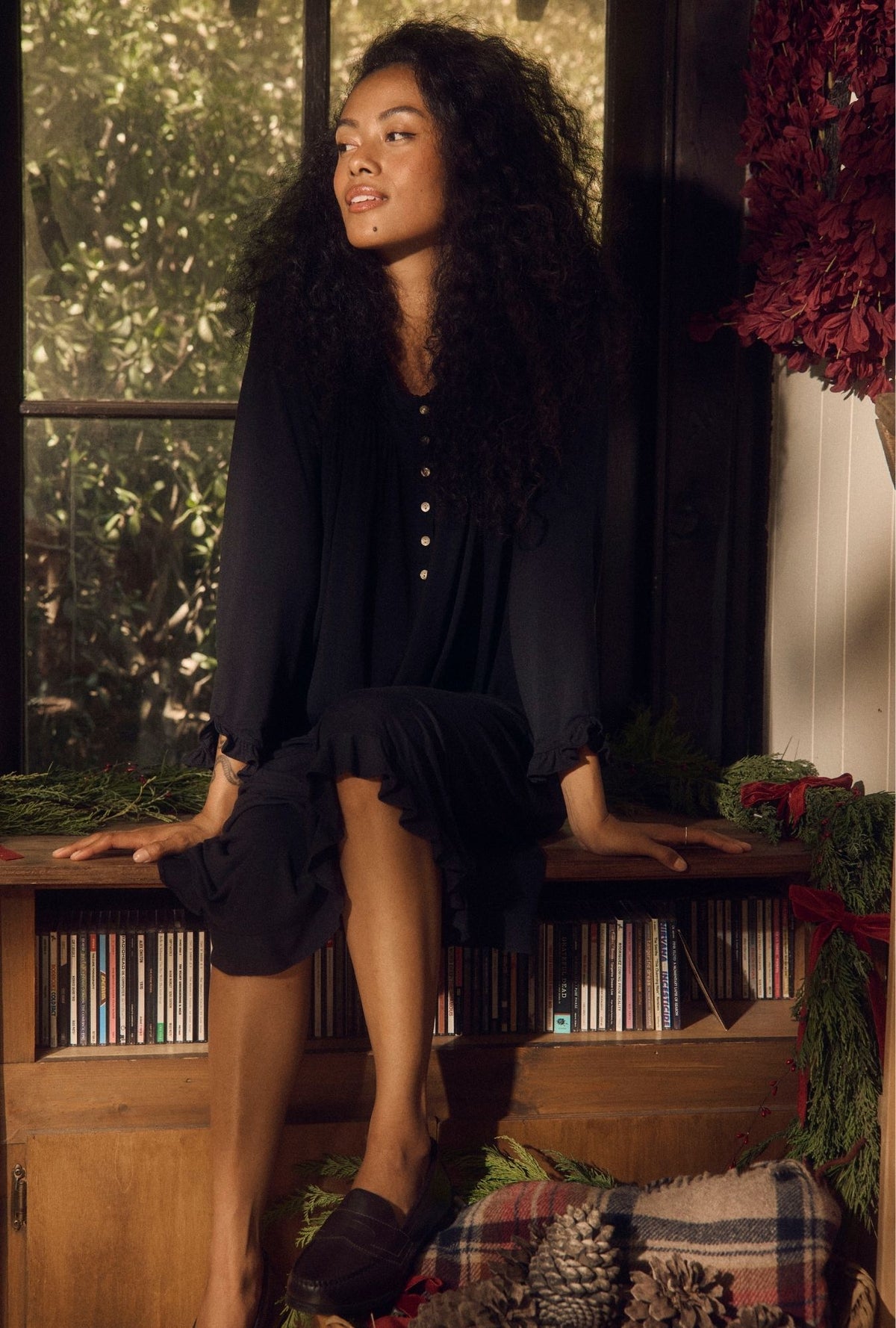 A lady wearing Iconic Black TENCEL™ Modal Spandex Jersey Knit Long Sleeve Waltz Nightgown sitting on a shelf looking sideways. 