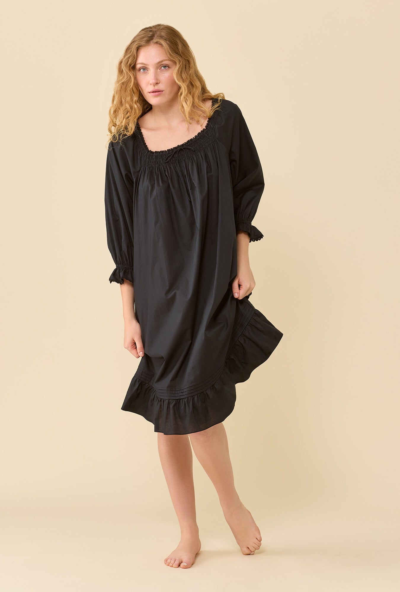 A lady wearing Iris Iconic Black 100% Cotton Woven Lawn 3/4 Sleeve Waltz Nightgown holding the bottom