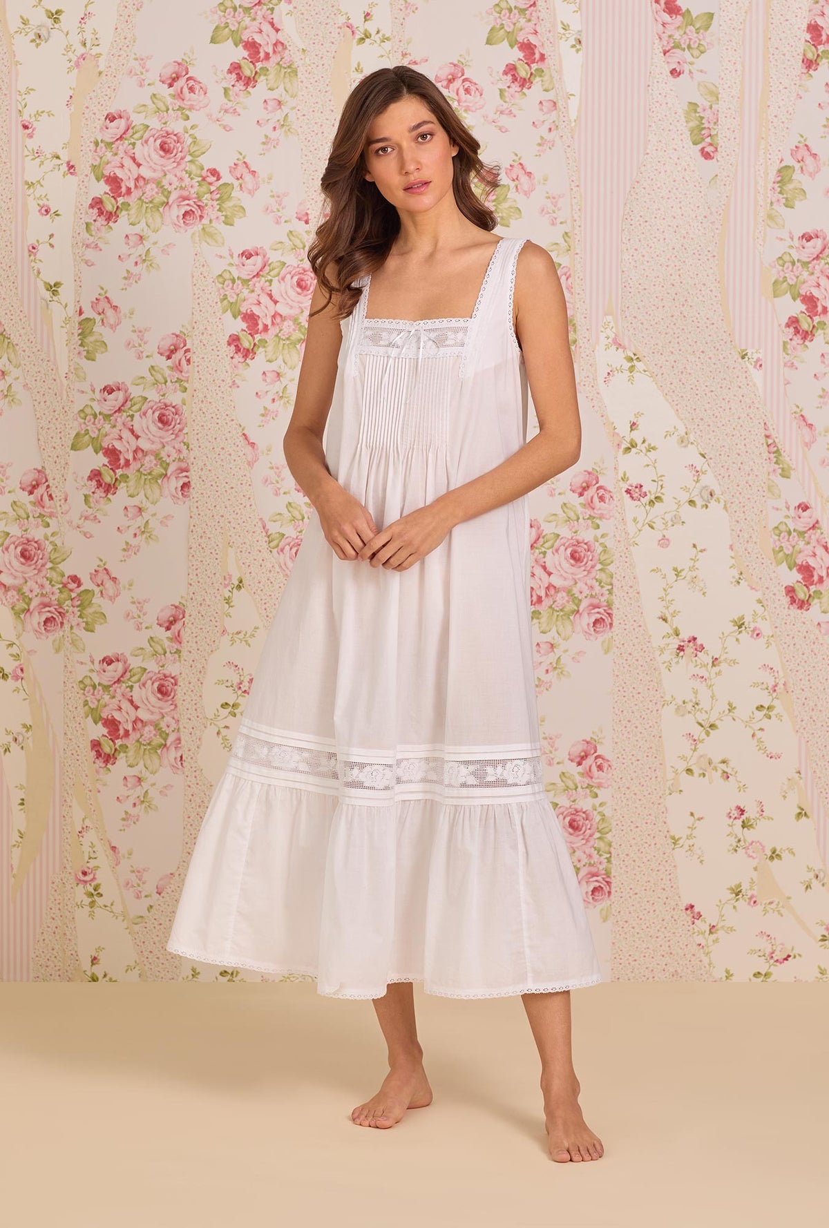 A Lady Wearing The "Adrianna" Iconic White Cotton Lawn Ballet Nightgown facing front in a sightly angled pose with placing her hands in front of her body