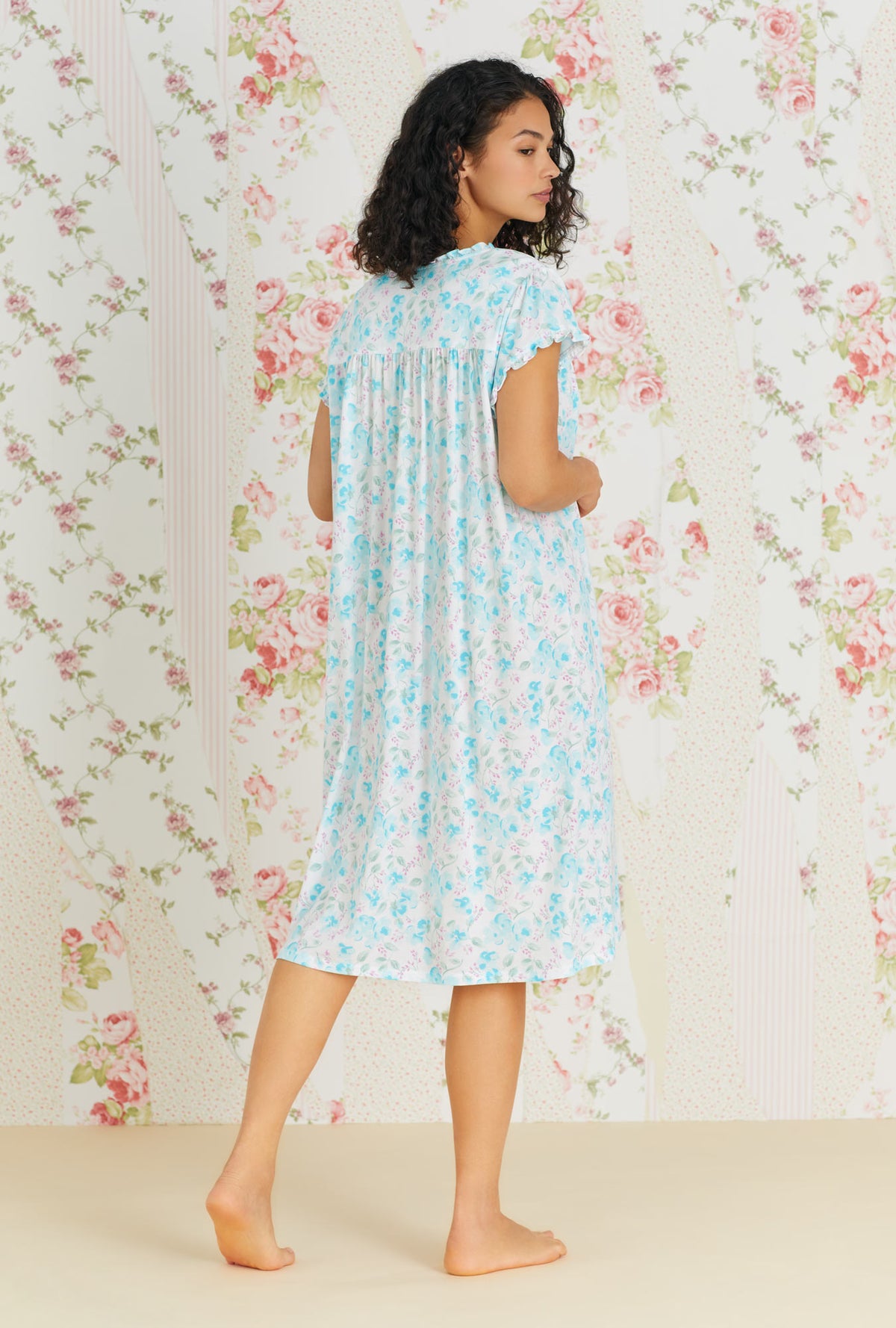 A lady wearing a white and aqua cap sleeve waltz knit nightgown with primrose garden print.