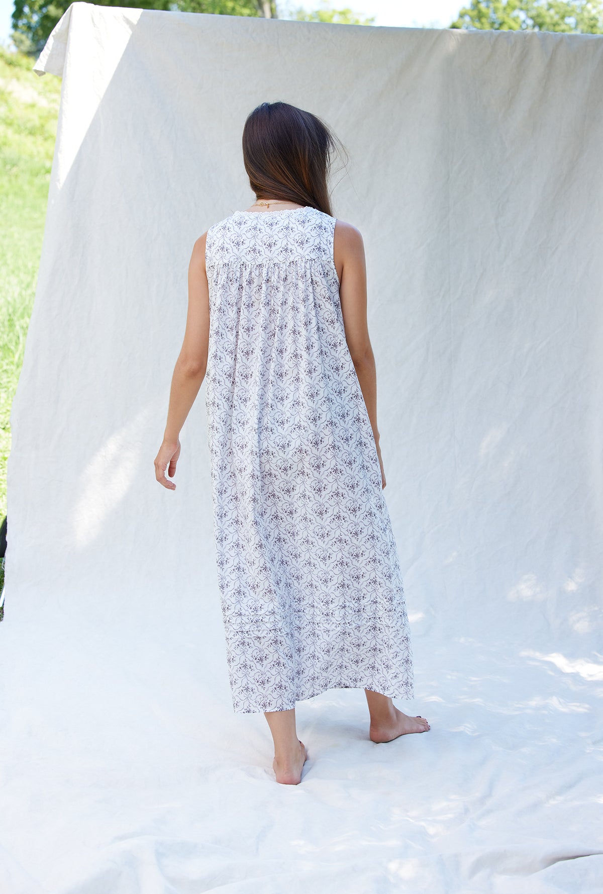 A lady wearing a white sleeveless grey ribbon floral cotton nightgown.