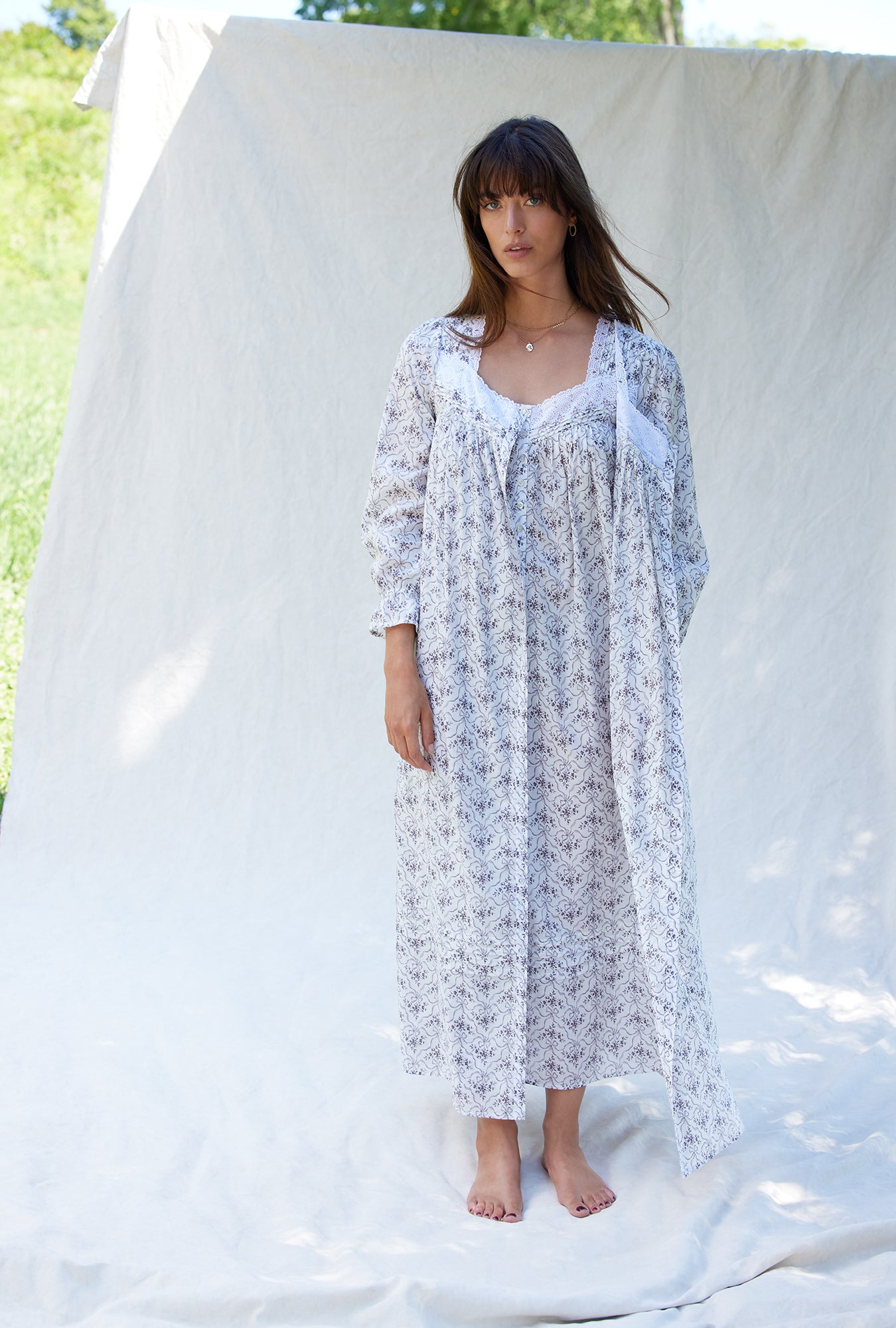 A lady wearing a white long sleeve grey ribbon floral cotton button front robe.