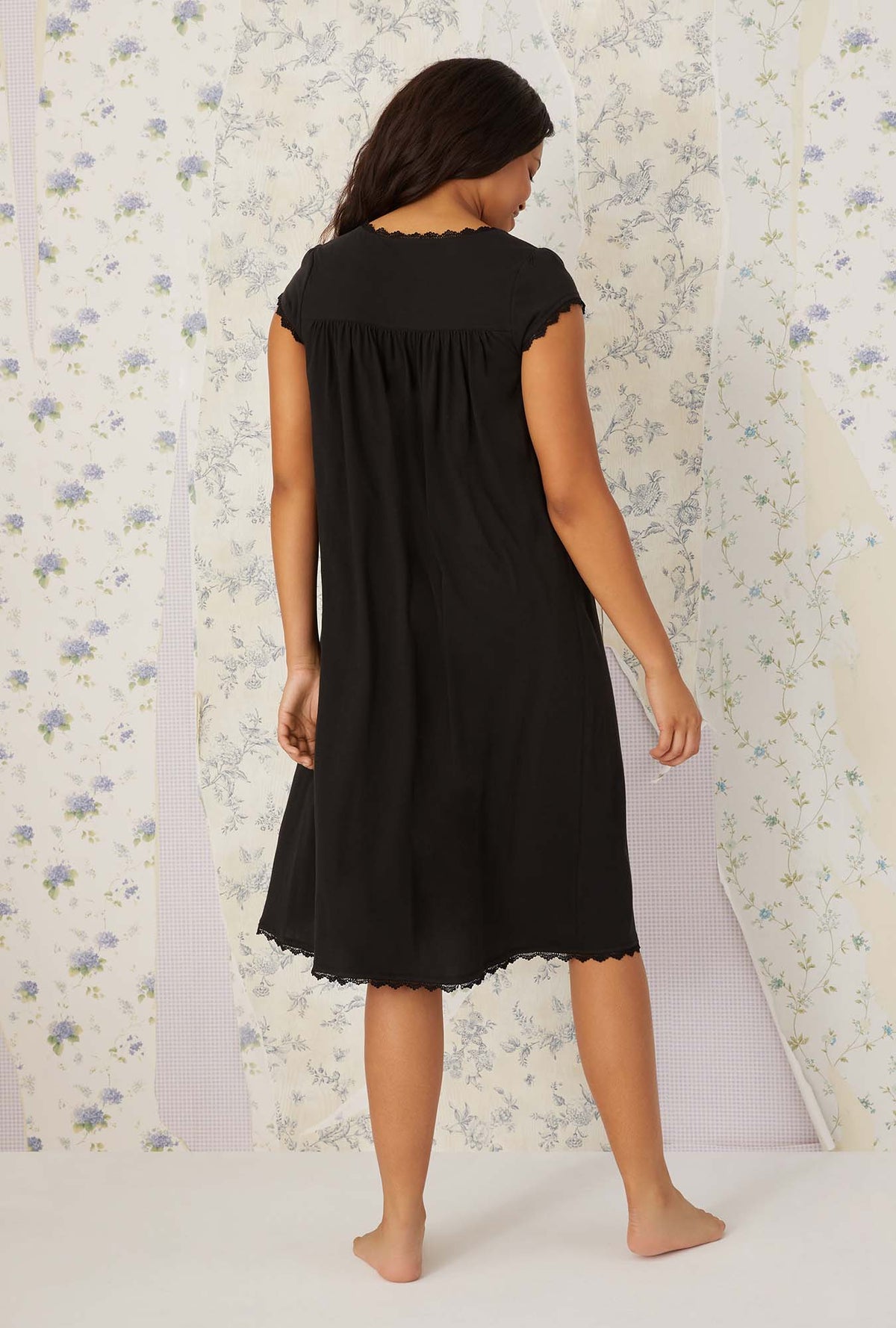 A lady wearing plus size black villa blanca waltz knit nightgown in a back view pose