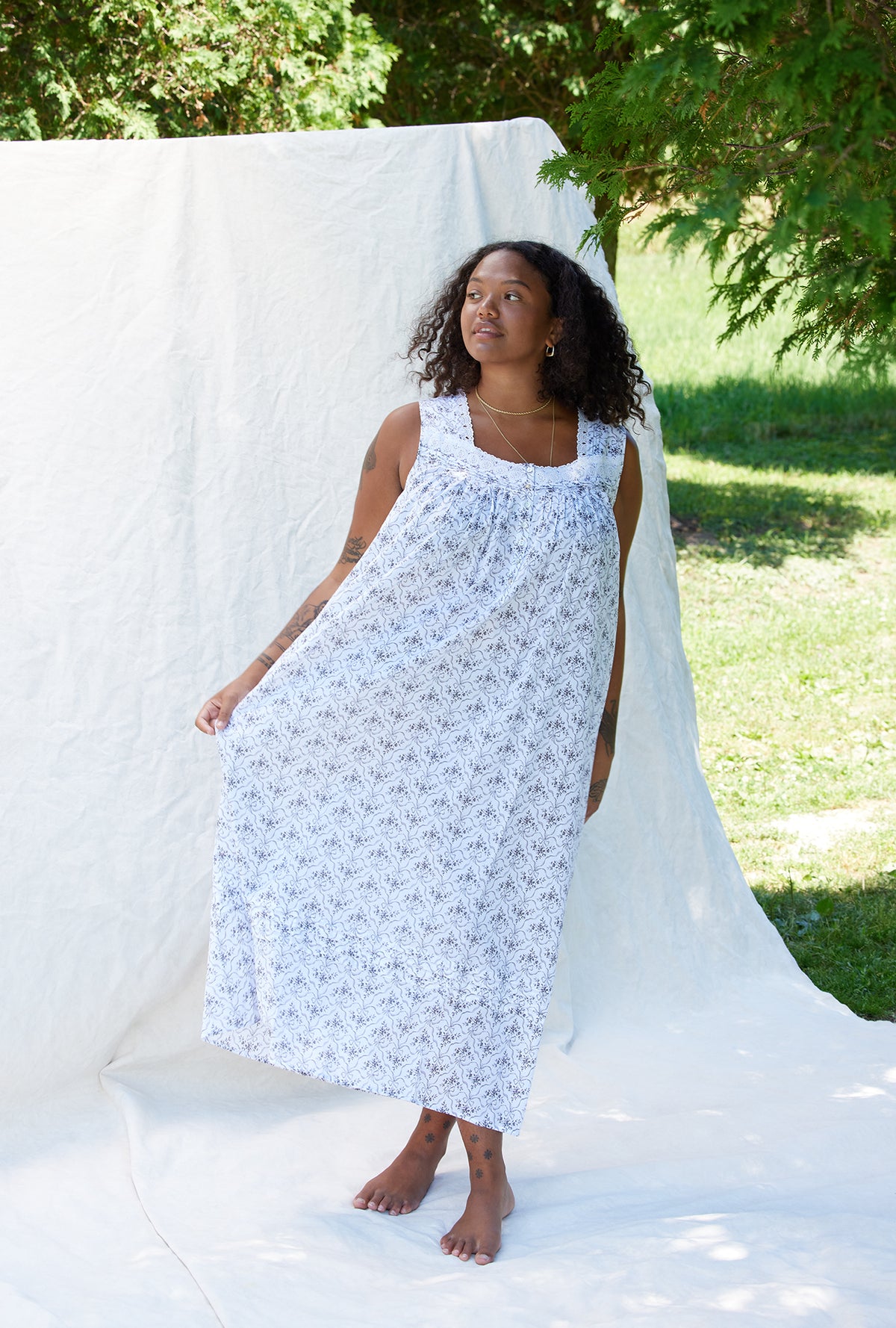 A lady wearing a white sleeveless grey ribbon floral cotton nightgown.